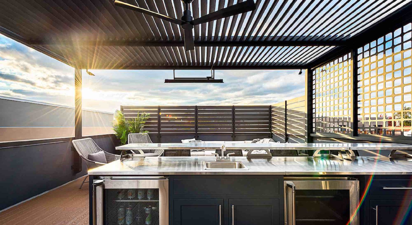 Linear outdoor kitchen on a rooftop patio with a stainless countertop, built-in sink, refrigerator drawers, and overhead heater